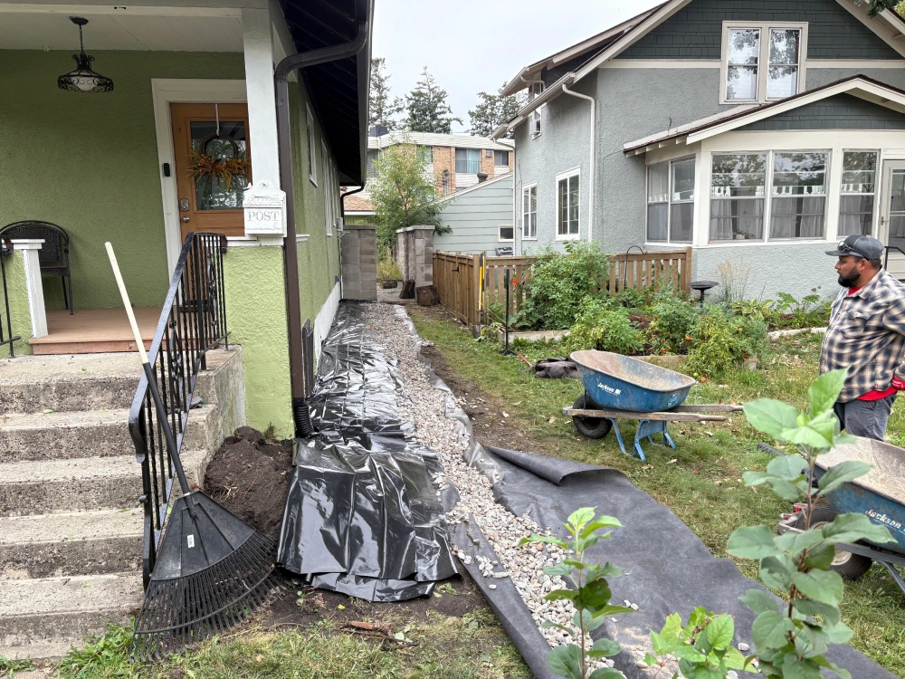 French Drain Installation Along Foundation — During French drain installation in progress along home foundation with gravel bed drain pipe and landscape fabric visible