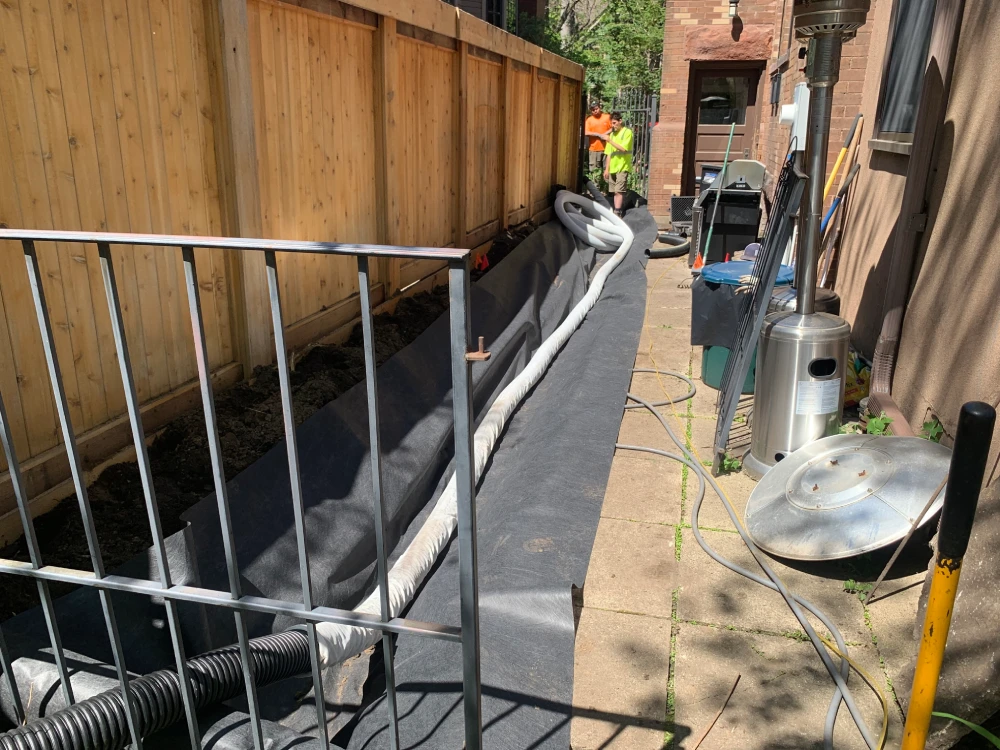 French Drain Pipe and Landscape Fabric Being Installed Perforated drain pipe and landscape fabric laid in trench during french drain installation by John's Pro Care